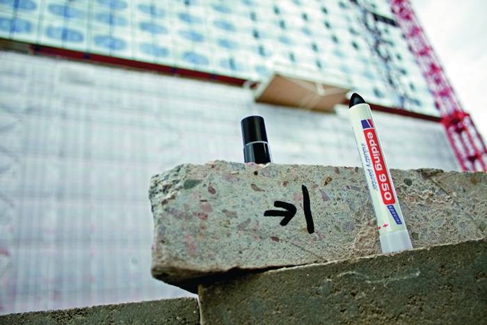 Eine Baustelle mit einem Ziegel, der von einem Pfeil markiert ist. Daneben befindet sich ein großer weißer Marker mit der Aufschrift 