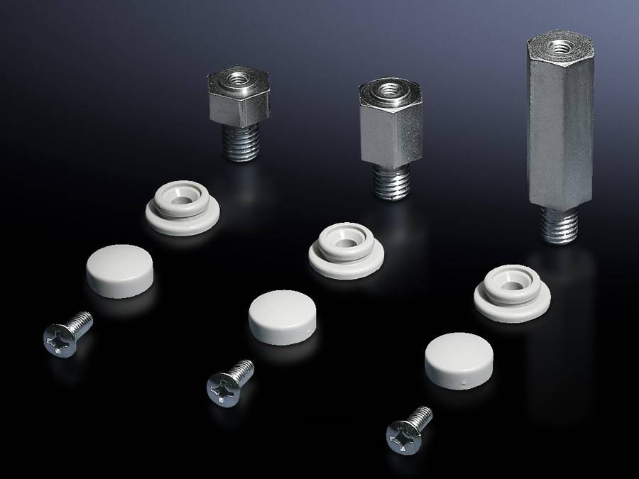 Metallabstandshalter und Unterlegscheiben, die in parallelen Linien auf einem dunklen Hintergrund angeordnet sind, mit Schrauben am unteren Bildrand, was eine Montage von Hardware andeutet.
