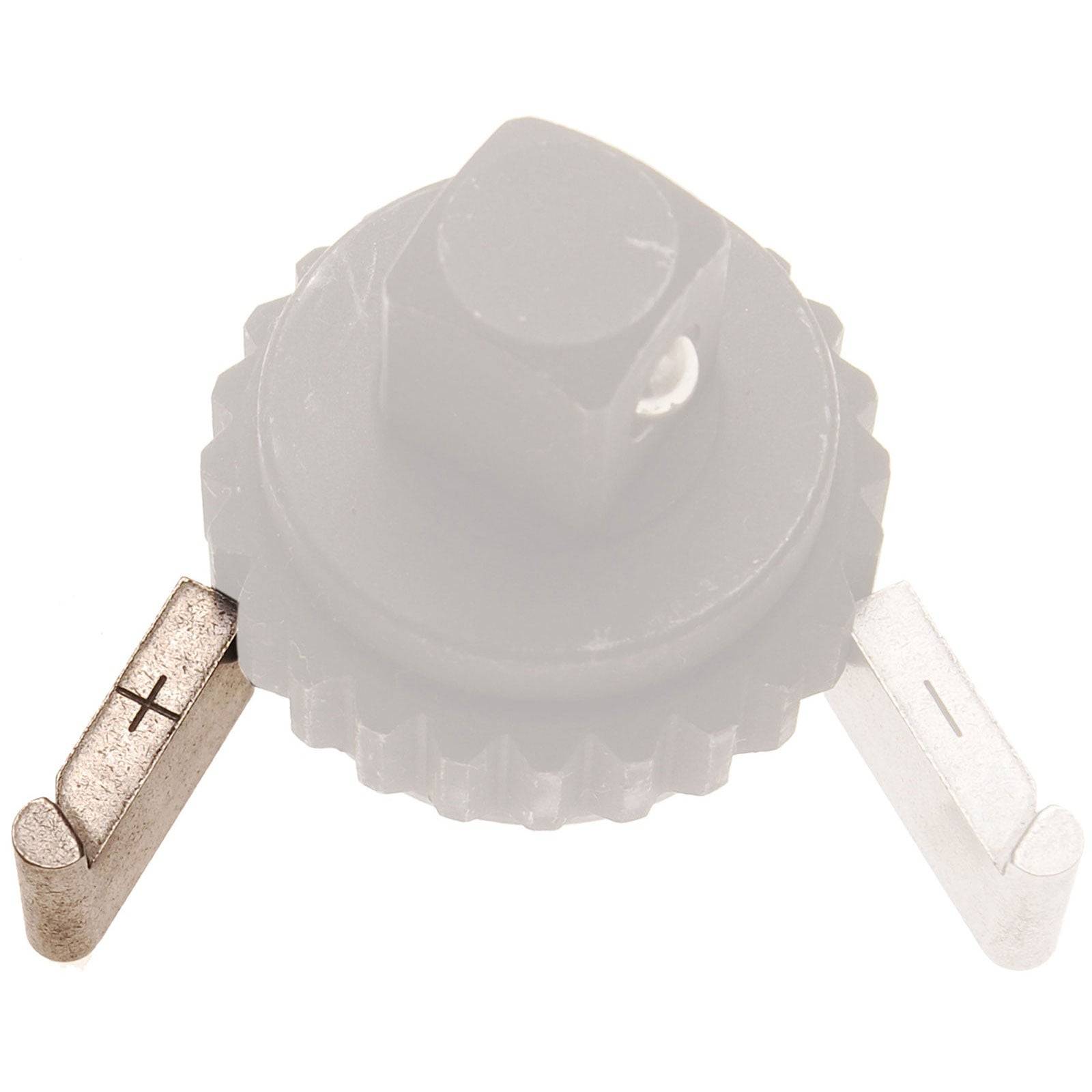 Ein rundes Zahnrad mit hervorstehenden Metallzacken auf gegenüberliegenden Seiten, gekennzeichnet mit Plus- und Minuszeichen.