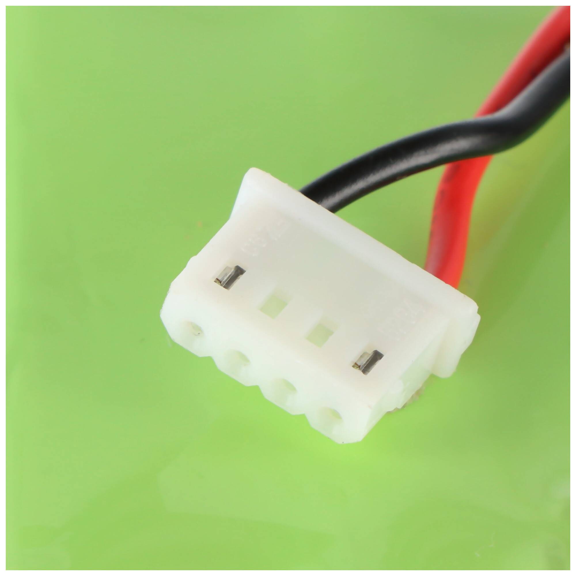 Nahaufnahme eines weißen dreipoligen Elektrosteckers mit roten und schwarzen Kabeln vor grünem Hintergrund.