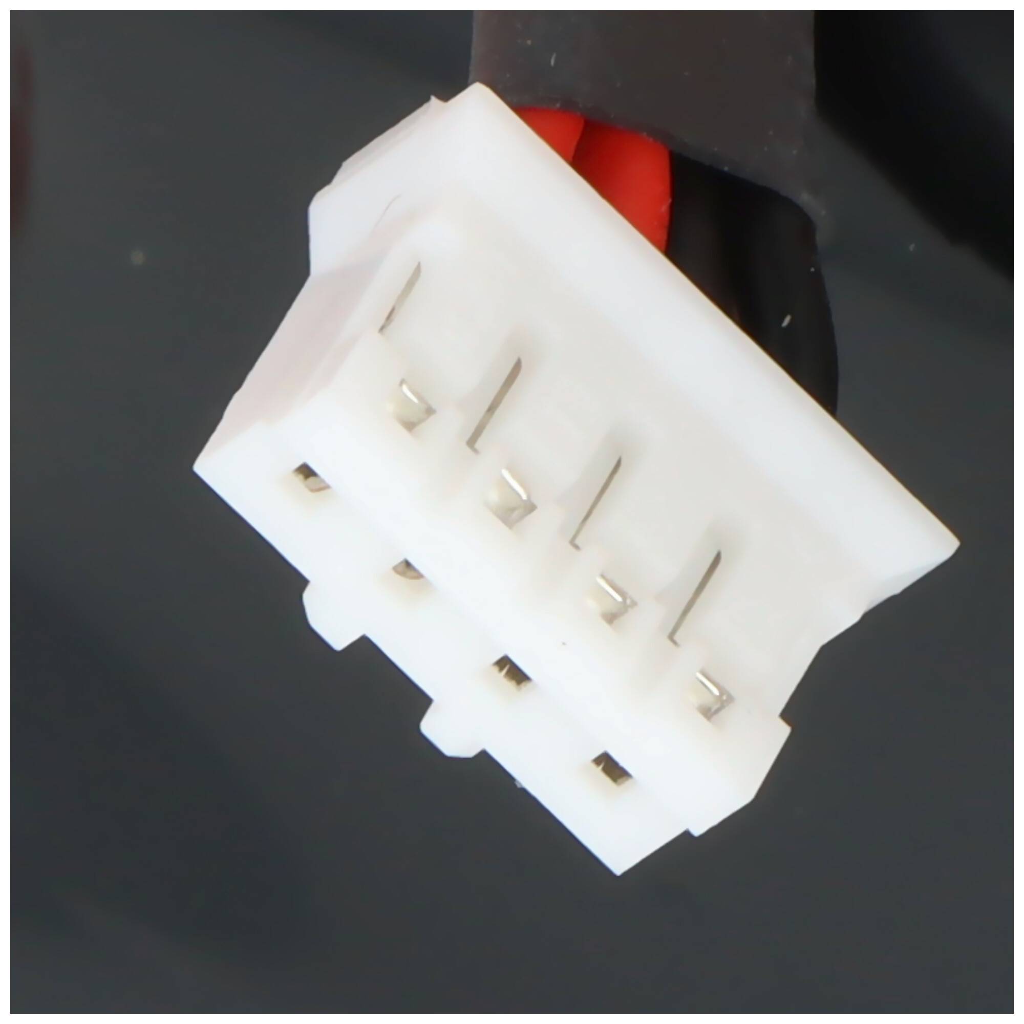 Nahaufnahme eines weißen mehrstiftigen Elektrosteckers mit einem roten Draht auf dunklem Hintergrund.