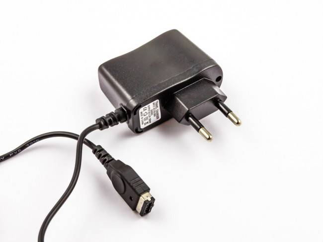 Schwarzer Stromadapter mit zweipoligem Stecker und angeschlossenem Kabel, das in einen kleinen Stecker auf weißem Hintergrund endet.