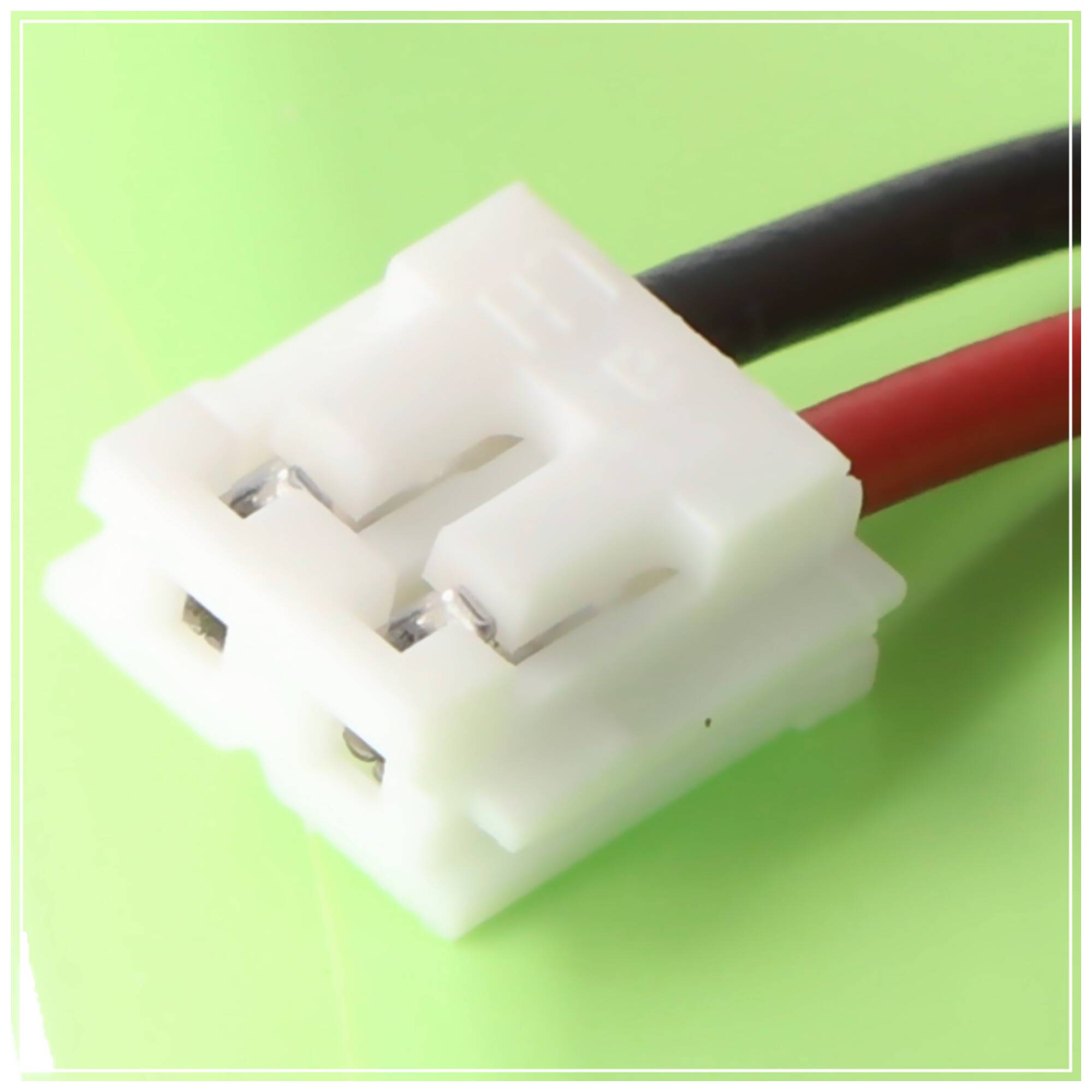 Nahaufnahme eines weißen zweipoligen Elektrosteckers mit roten und schwarzen Drähten auf grünem Hintergrund.