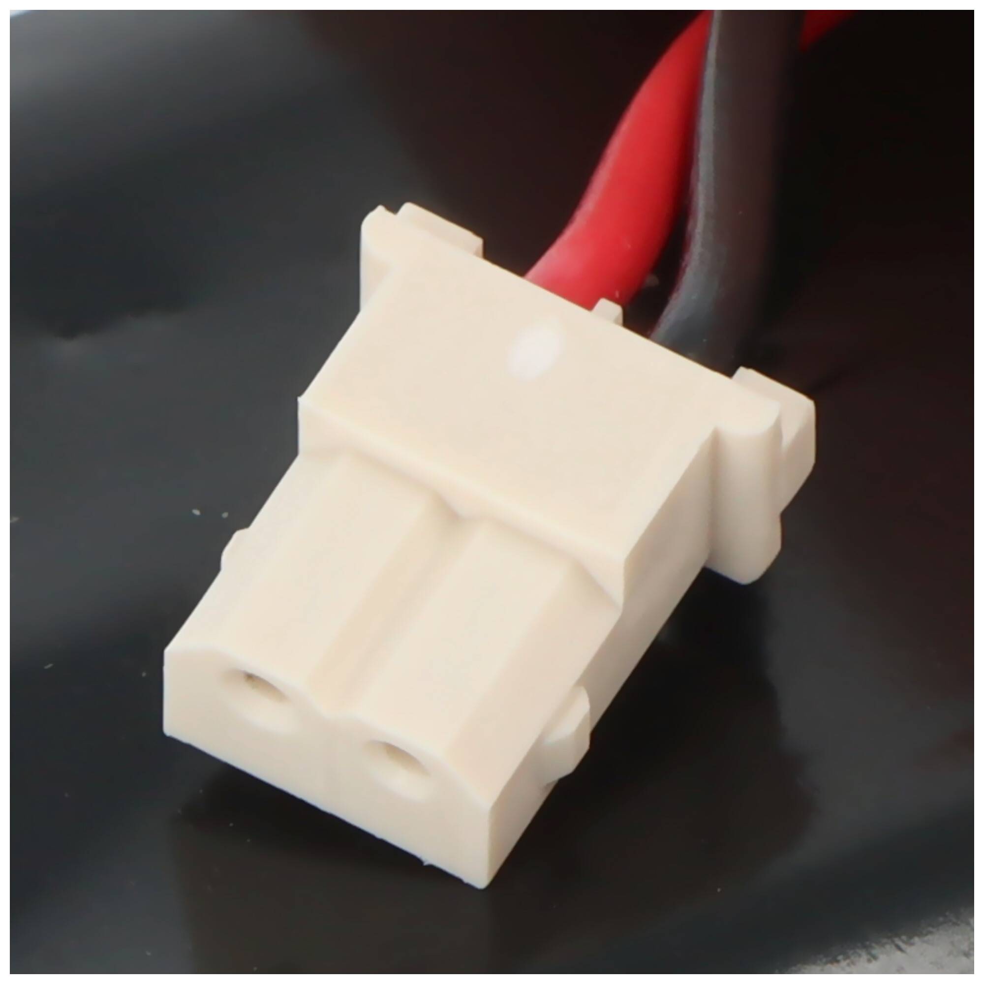 Weißer zweipoliger Elektrostecker mit rot und schwarz gefärbten Drähten auf einer dunklen Oberfläche angebracht.