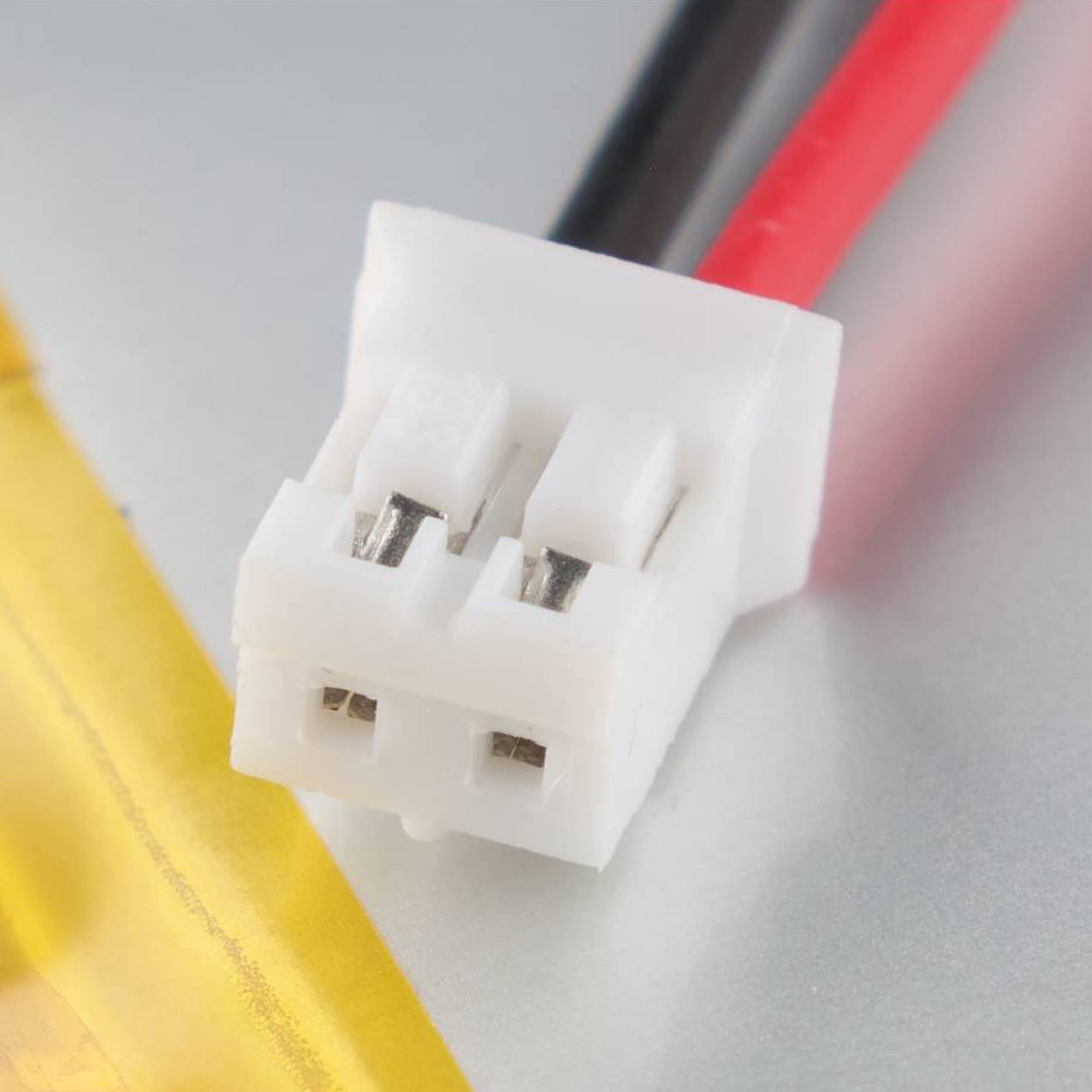 Nahaufnahme eines weißen zweipoligen Elektrosteckers mit angeschlossenen roten und schwarzen Kabeln auf einer hellen Oberfläche.