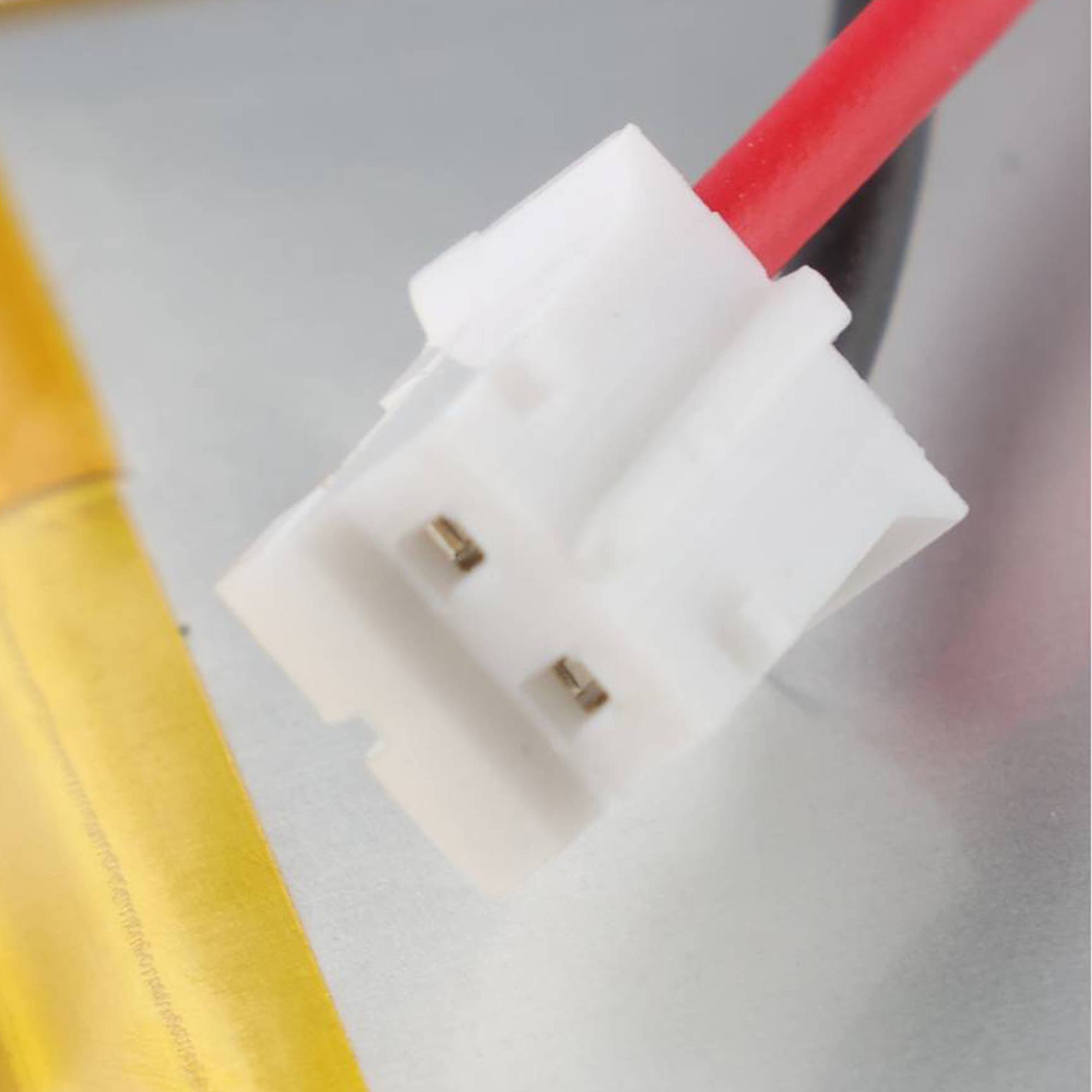 Nahaufnahme eines weißen zweipoligen Steckverbinders, der an roten Drähten neben einer gelben Batteriezelle angebracht ist.