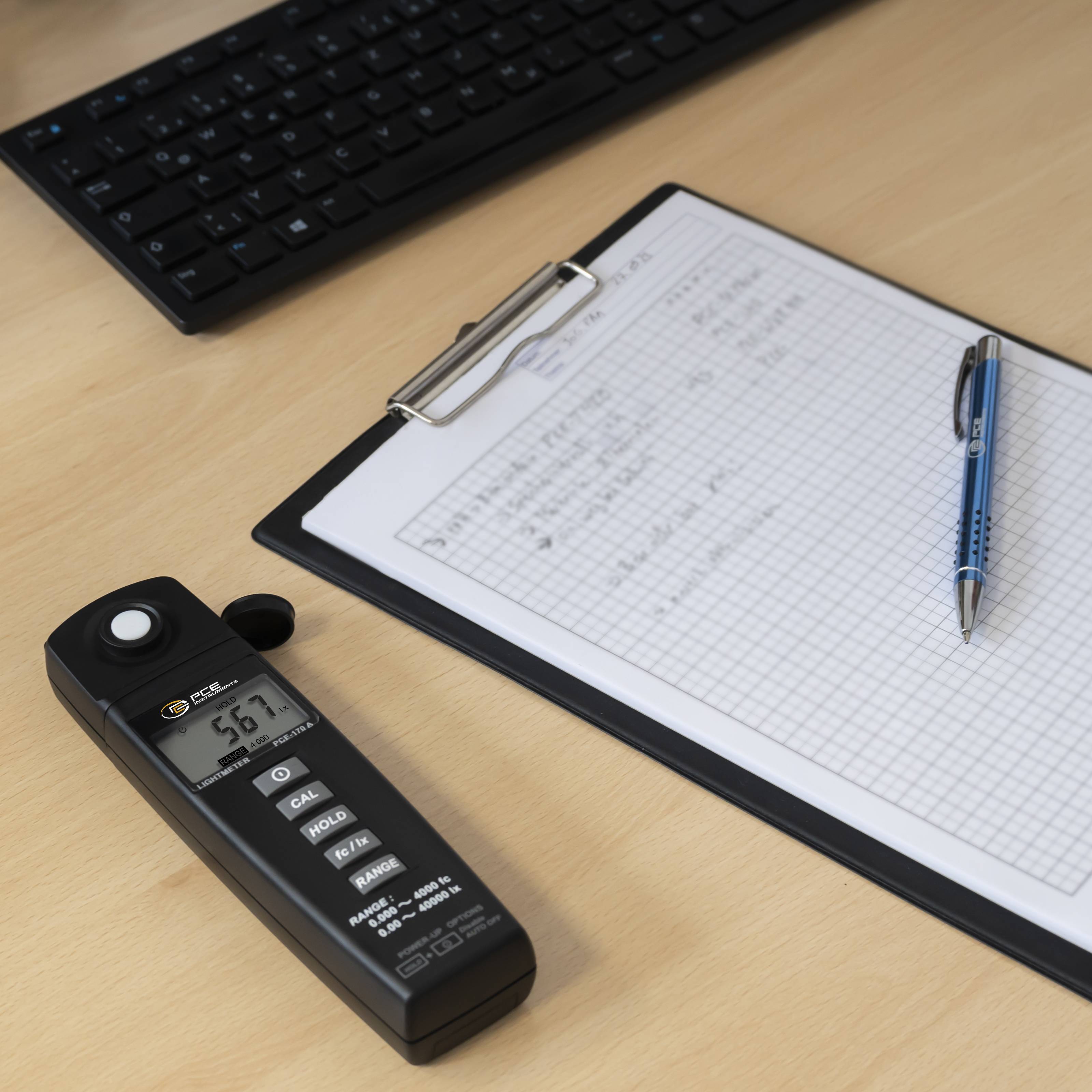 Ein Klemmbrett mit Millimeterpapier, das Notizen enthält, und ein blauer Stift darauf. Daneben befindet sich ein tragbares elektronisches Gerät, das 