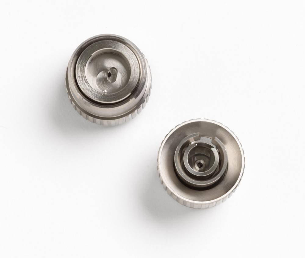Zwei metallische mechanische Komponenten mit kreisförmigen Rillen und Einkerbungen, nebeneinander auf einem weißen Hintergrund positioniert, höchstwahrscheinlich Bauteile für eine Montage.