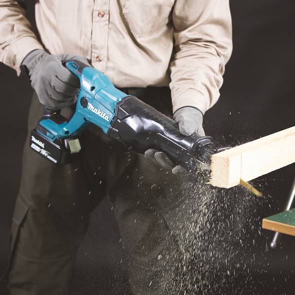 Person mit einer Makita Akku-Säbelsäge beim Schneiden eines Holzbretts, wobei Sägespäne aus dem Schnittende spritzen.