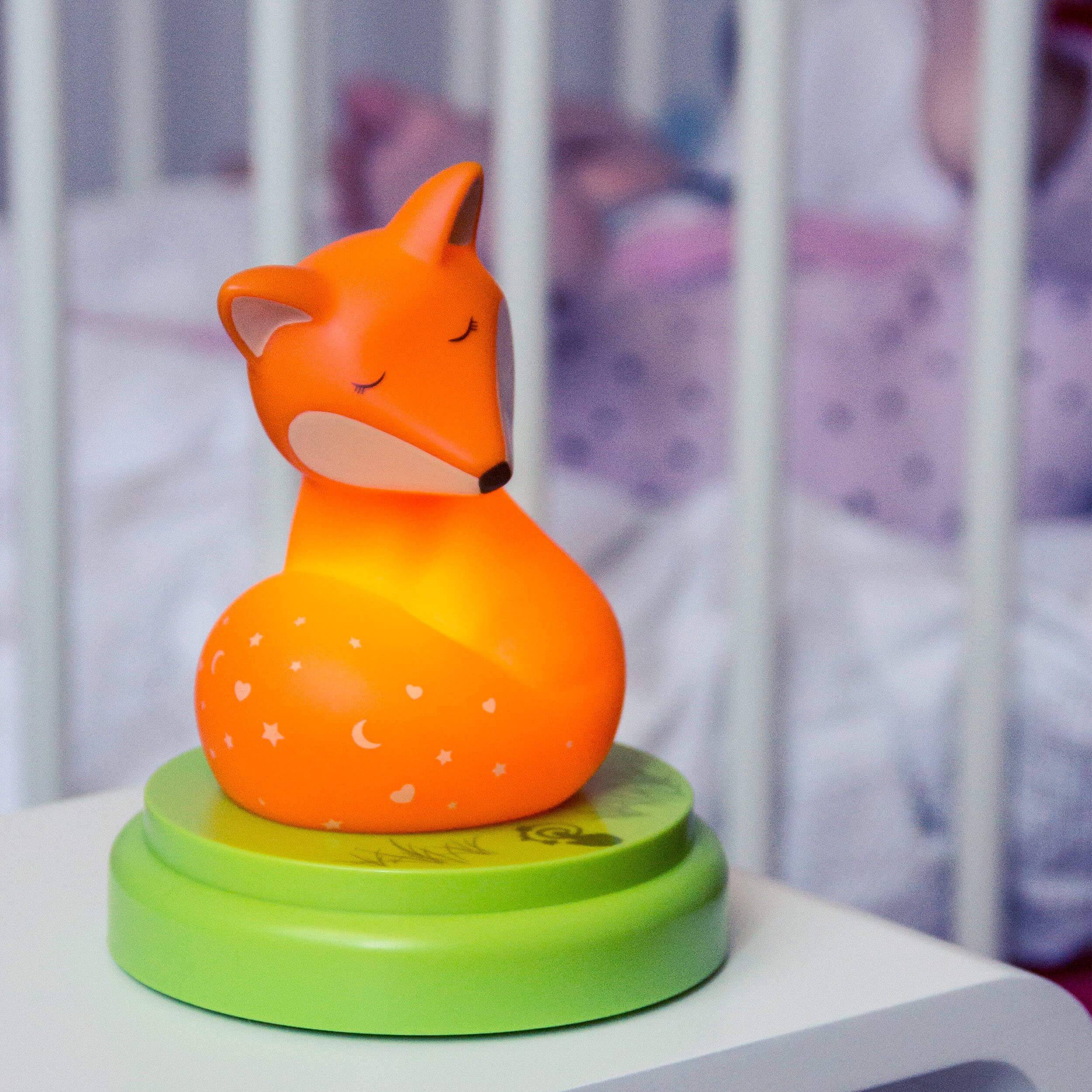 Orange Fuchs-förmiges Nachtlicht auf grüner Basis, mit geschlossenen Augen, sitzt auf einem Nachttisch im Kinderzimmer.