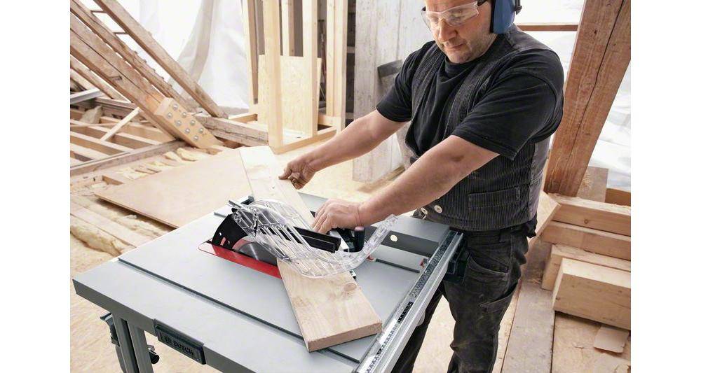 Eine Person mit Sicherheitsausrüstung verwendet eine Kreissäge, um ein Holzstück in einer Werkstatt zu schneiden und dabei Holzbearbeitungsfähigkeiten und Sicherheitspraktiken zu demonstrieren.