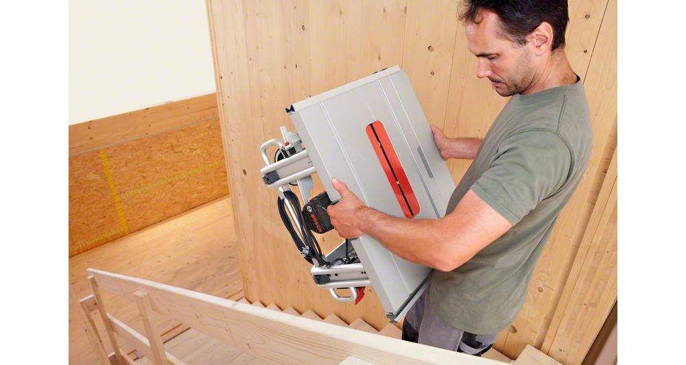 Eine Person installiert einen Treppenlift an einer Holztreppe und konzentriert sich dabei auf die Einstellung des Plattformmechanismus.