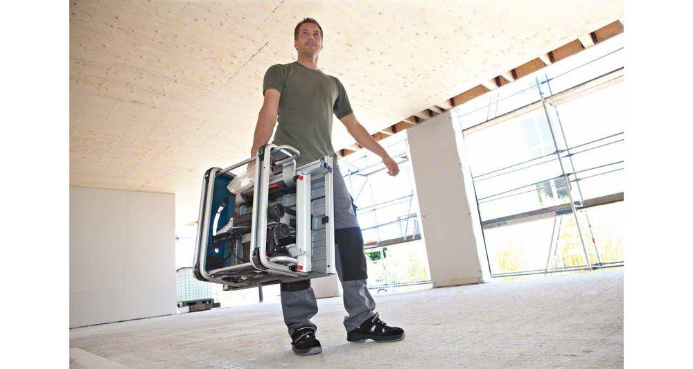 Eine Person trägt eine kompakte Kreissäge in ein im Bau befindliches Gebäude mit unfertigen Wänden und einer unfertigen Decke und unterstreicht damit deren Tragbarkeit.