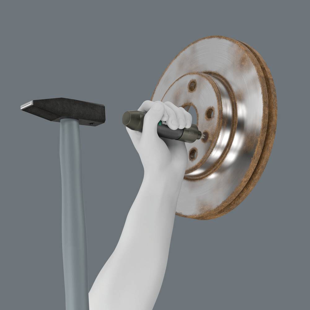 Weiß behandschuhte Hand, die ein Werkzeug gegen ein rostiges Metallrad oder eine rostige Metallscheibe hält, neben einem Hammer, was auf Reparatur oder Wartung hindeutet.