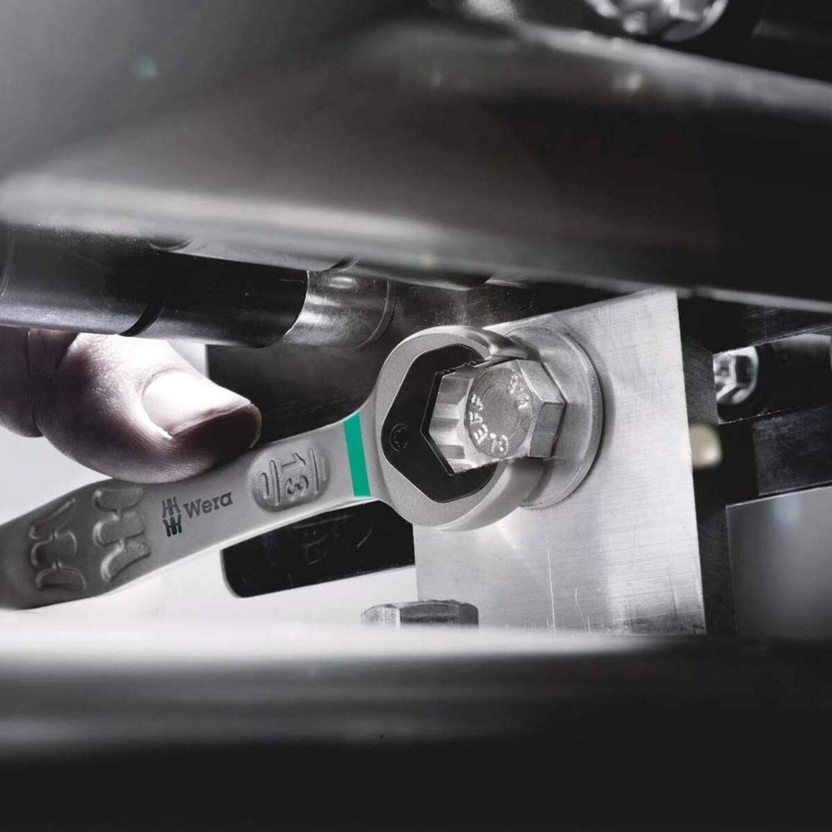 Hand, die einen Wera-Schraubenschlüssel verwendet, um einen Bolzen an einer Metallmaschinenkomponente einzustellen und dabei die Anwendung des Werkzeugs in mechanischen Umgebungen hervorhebt.