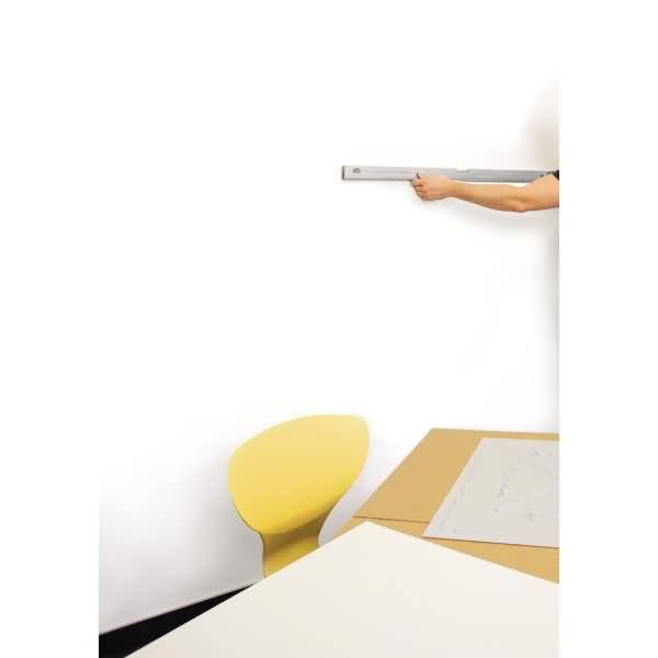 Eine Person benutzt ein langes Wasserwaagenwerkzeug gegen eine weiße Wand über einem Stuhl und Tisch mit Plänen, was auf Mess- oder Aufhängungsarbeiten hindeutet.