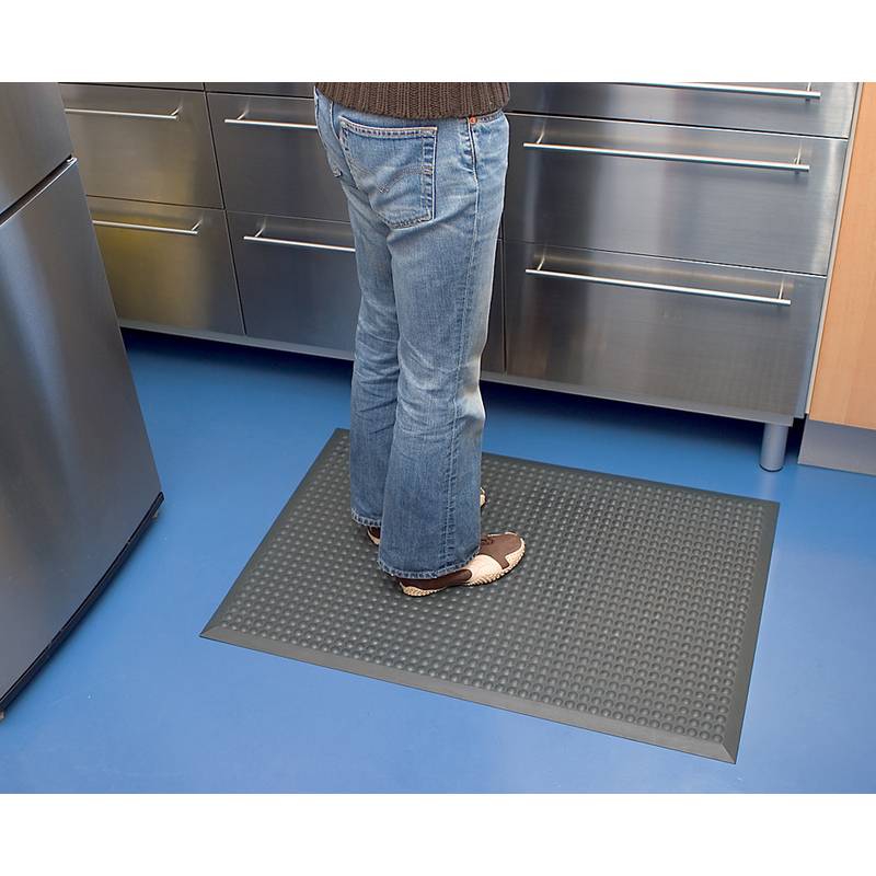 Eine Person steht auf einer strukturierten Anti-Ermüdungsmatte in einer Küche mit Edelstahlschränken und blauem Boden.
