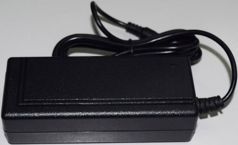 Ein schwarzes Laptop-Ladegerät mit sichtbarem Netzkabel, das auf einer weißen Oberfläche liegt.