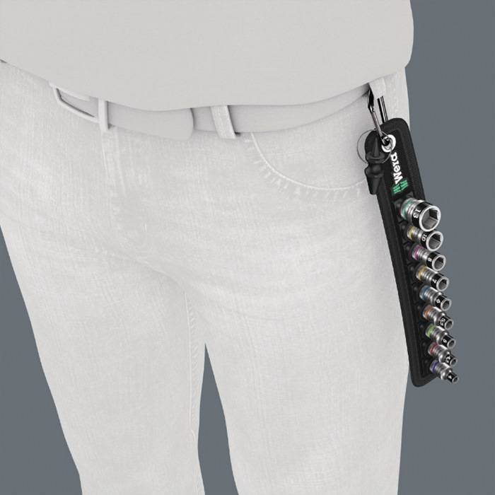 Eine Person, die helle Hose trägt, mit einem Clip an einer Gürtellassche, und einen Satz metallischer Sechskantschlüssel hält.