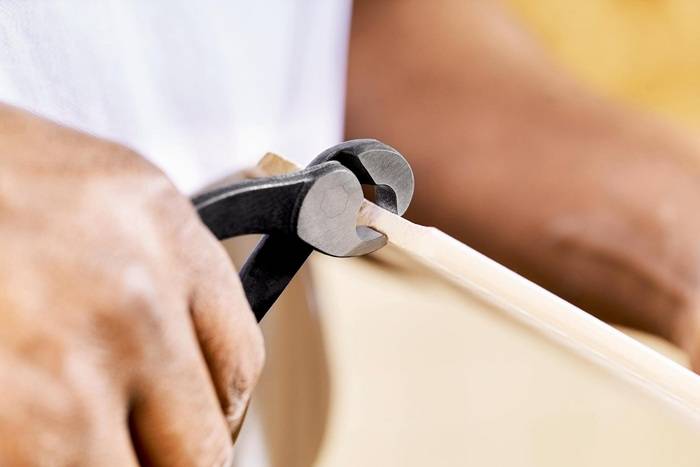 Eine Nahaufnahme einer Hand, die mit einer Drahtschere einen dünnen Holzdübel präzise zuschneidet und damit handwerkliches Geschick demonstriert.