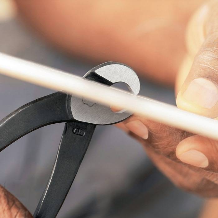 Eine Hand greift ein Paar Zangen, um einen dünnen Draht zu durchtrennen. Der Fokus liegt auf der Schneidaktion und dem Werkzeug.