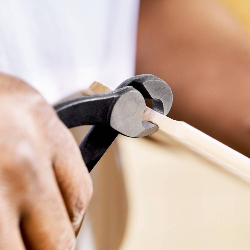 Eine Person verwendet ein Paar Zangen, um an einem Holzobjekt zu arbeiten und sich dabei auf Präzision und Details in einer Holzbearbeitungsaufgabe zu konzentrieren.