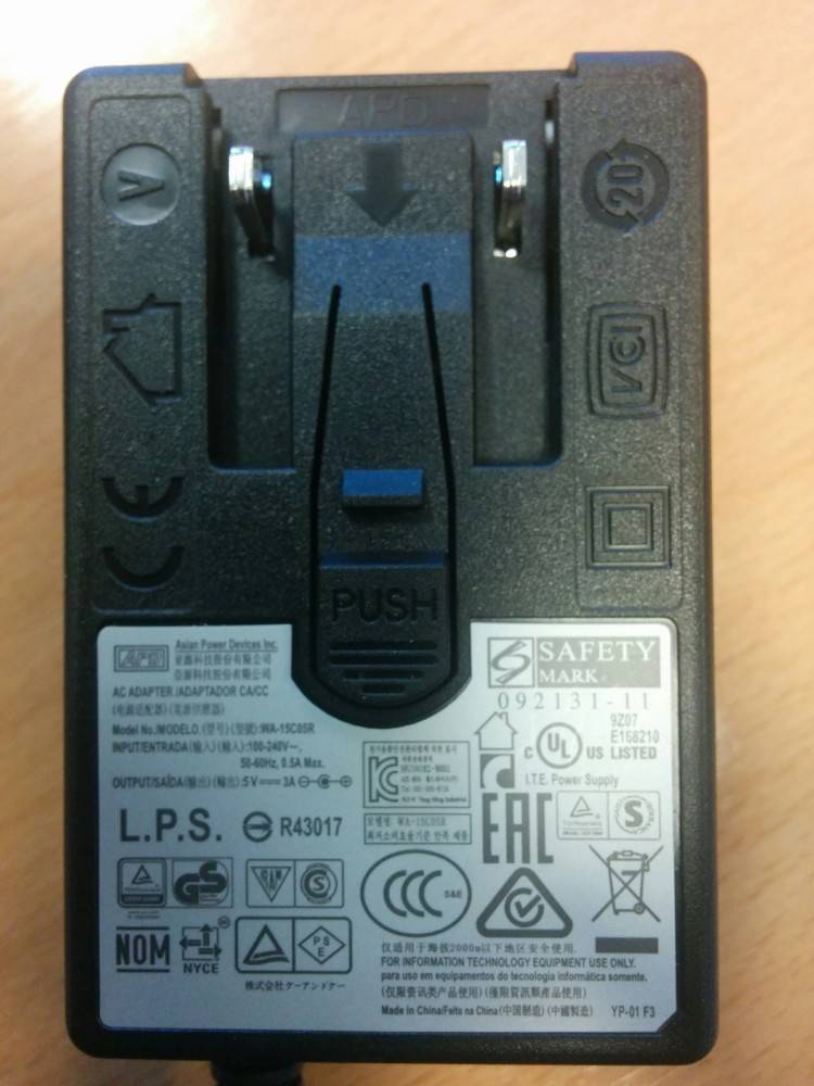 Netzteil-Nahaufnahme mit Sicherheitszertifizierungen wie SAFETY MARK und UL US LISTED, mit Symbolen, die Leistungseingangs- und -ausgabedetails angeben.