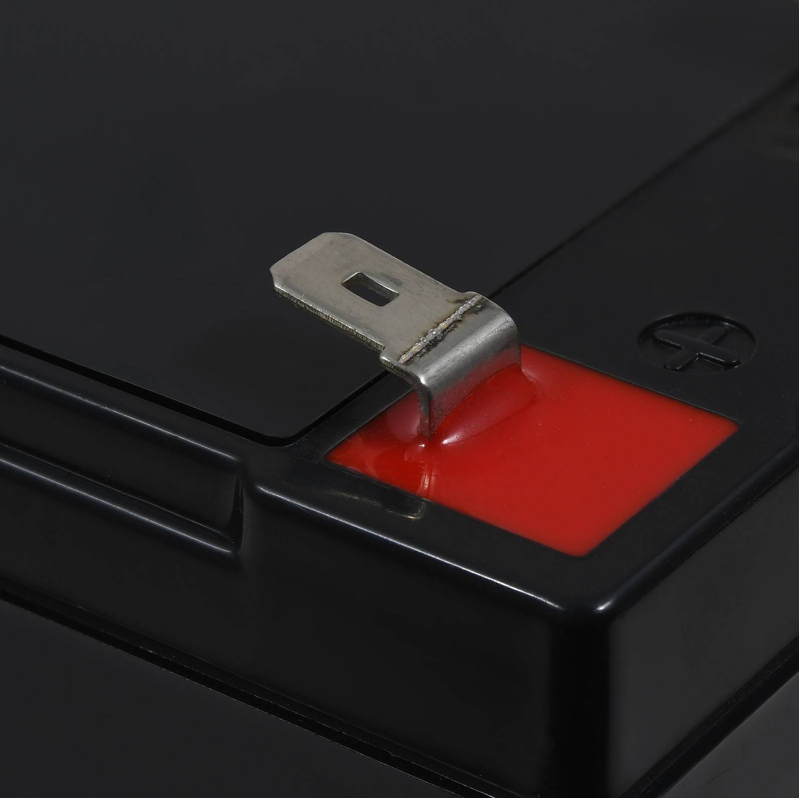 Nahaufnahme eines Batterieanschlusses mit einem roten Plusanschluss und einer Metalllasche auf einem schwarzen Batteriegehäuse.