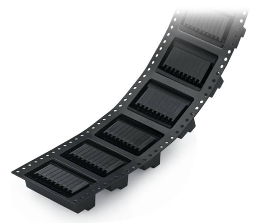 Ein Streifen elektronischer Bauteile in schwarzer Verpackung, der zur Montage in der Fertigung verwendet wird, vor einem schlichten Hintergrund.