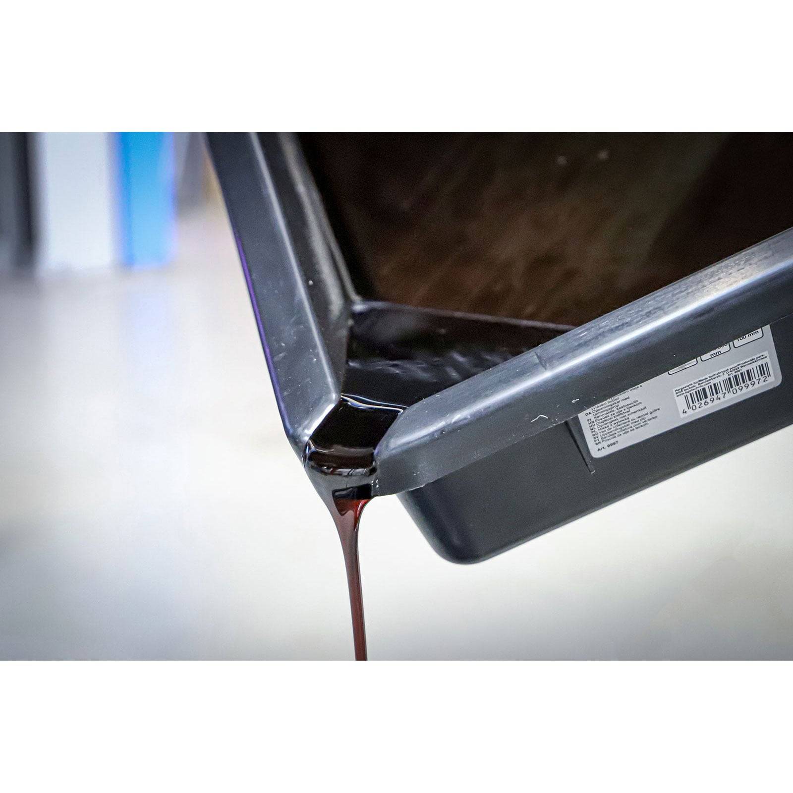 Öl tropft aus der Ecke eines schwarzen Tabletts auf den Boden in einer Garagenumgebung.