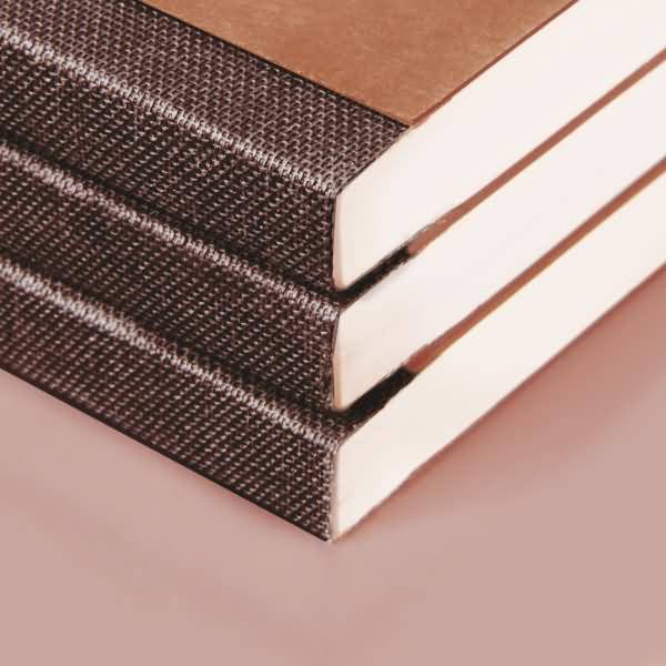 Drei gestapelte Hardcover-Bücher mit dunklen strukturierten Rücken und weißen Seiten auf rosafarbenem Hintergrund.