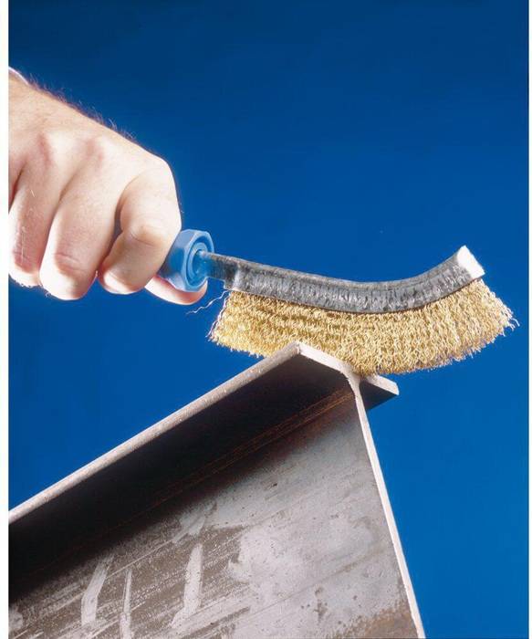 Eine Hand benutzt eine Drahtbürste, um eine Metalloberfläche vor einem blauen Hintergrund zu reinigen.