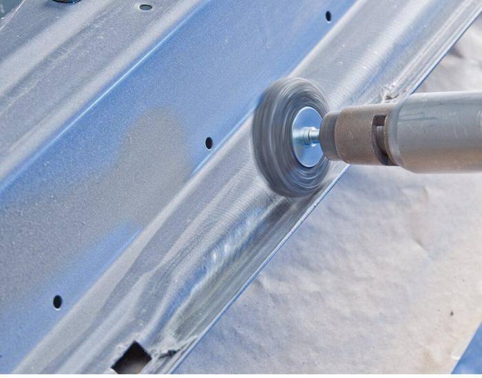 Eine Motorsäge schleift eine Metalloberfläche ab und erzeugt dabei Funken, mit einem blauen Metallblech als Hintergrund.