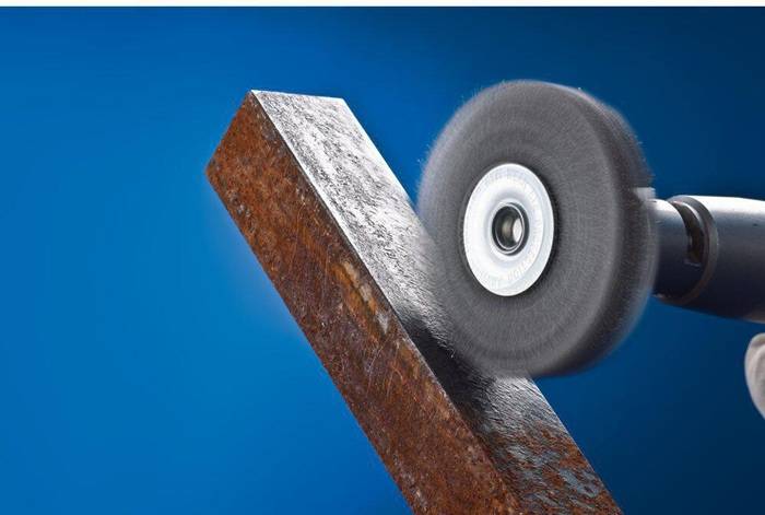 Eine Trennschleifmaschine mit einer rotierenden Schleifscheibe bearbeitet die Kante eines rostigen Metallträgers vor einem blauen Hintergrund.