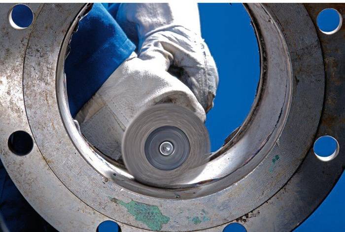Ein Arbeiter mit Handschuhen verwendet eine Kreissäge, um Metall zu durchtrennen, vor einem klaren blauen Himmel im Hintergrund.
