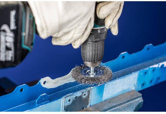 Eine Person, die eine Bohrmaschine mit einem Drahtbürstenaufsatz verwendet, um eine blaue Metalloberfläche zu reinigen oder zu polieren.