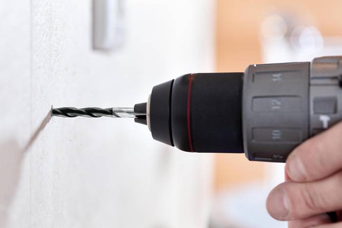 Ein kabelloses Bohrgerät bohrt in eine weiße Wand und der Fokus liegt auf dem Bohrereinsatz, der ein Loch macht.