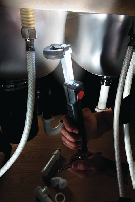 Eine Person, die mit einer Taschenlampe Rohre inspiziert und dabei den Fokus auf Wartungs- oder Reparaturarbeiten unter schlechten Lichtverhältnissen legt.