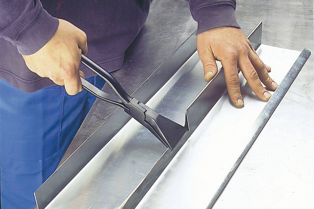 Ein Arbeiter biegt ein Metallblech mit Handwerkzeugen auf einer Biegepresse und formt die Kante entlang einer geraden Naht.