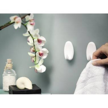 Eine Hand hält ein weißes Handtuch neben Wandhaken in einem spa-ähnlichen Badezimmer, mit Orchideenblüten und einer Seifenschale in der Nähe.