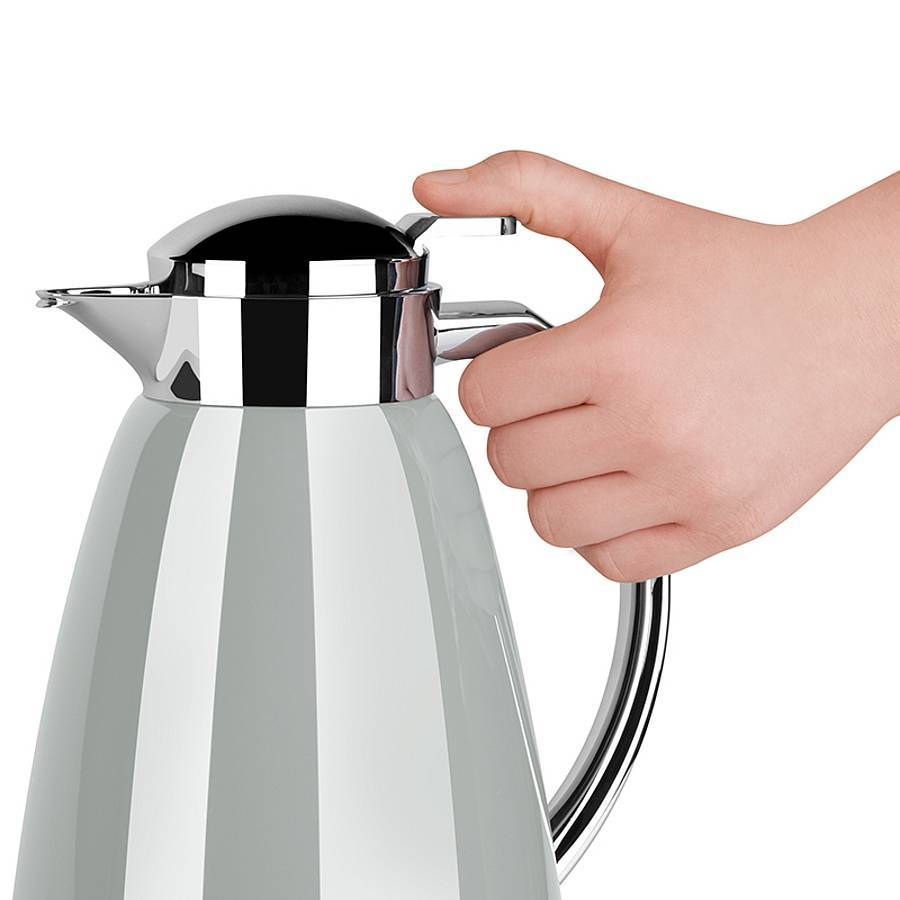 Hand drückt den Hebel an einer aus Edelstahl und Weiß isolierten Thermoskanne mit Griff und Ausguss auf neutralem Hintergrund.