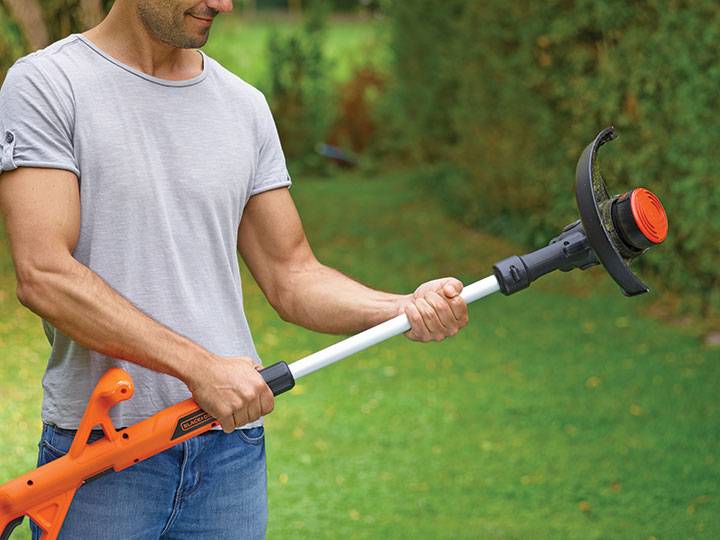 Ein Mann, der einen elektrischen Fadentrimmer verwendet, um Gras in einem Garten zu schneiden.