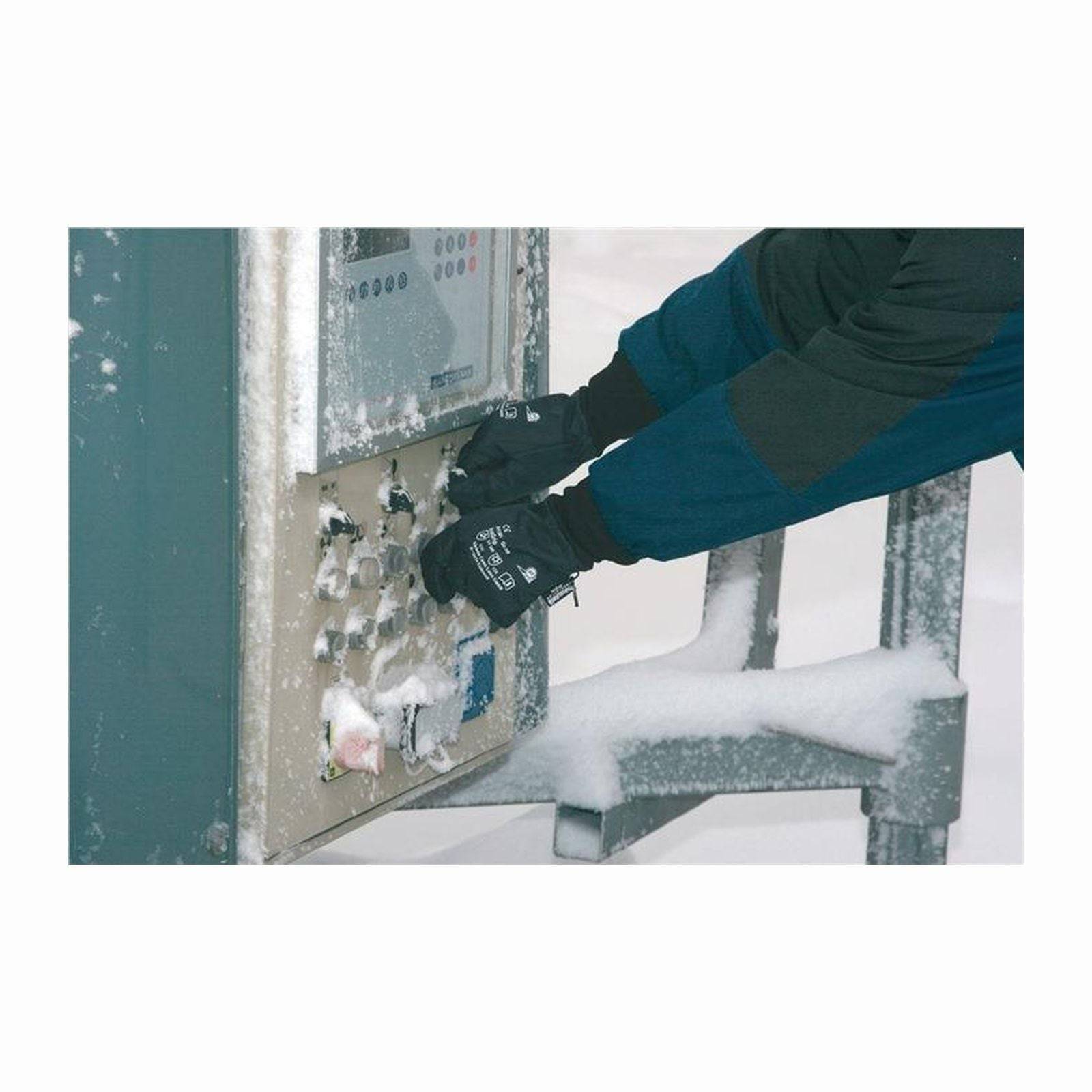 Person mit Handschuhen bedient einen schneebedeckten Fahrkartenautomat im Freien.