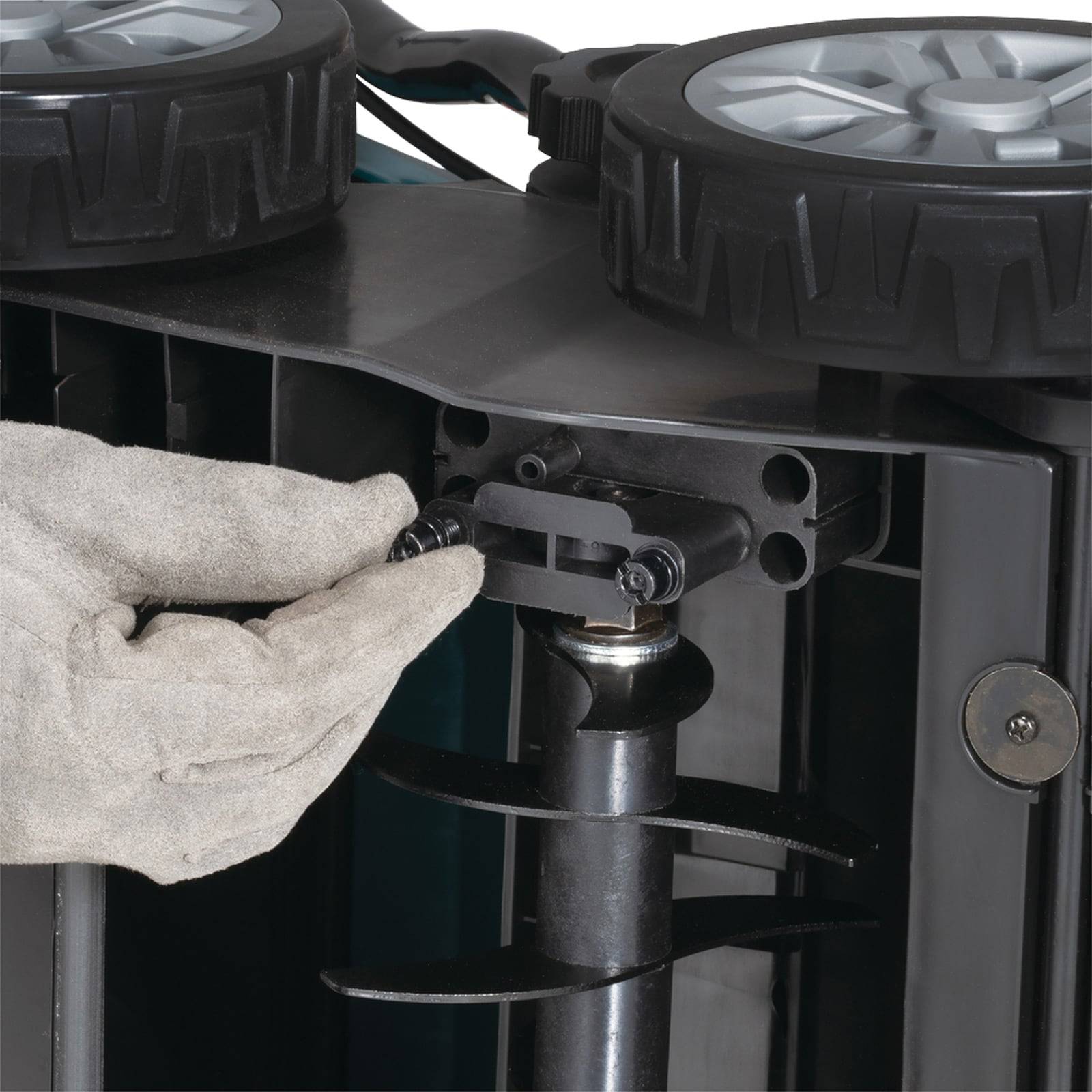 Eine behandschuhte Hand stellt eine Schraube an einem mechanischen Gerät mit großen Rädern ein, was auf Wartungs- oder Montagearbeiten hindeutet.