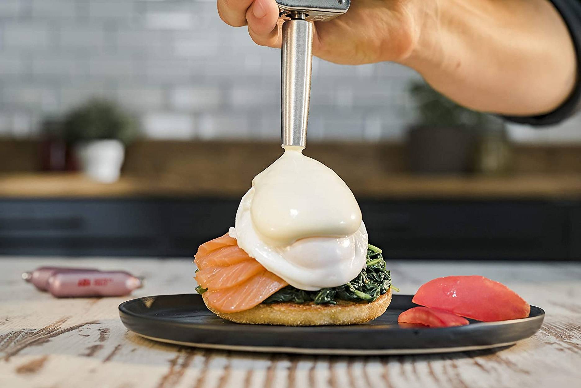 Der Chef legt ein pochiertes Ei auf Lachs-Toast auf einen schwarzen Teller, mit rosa Garnierung daneben.