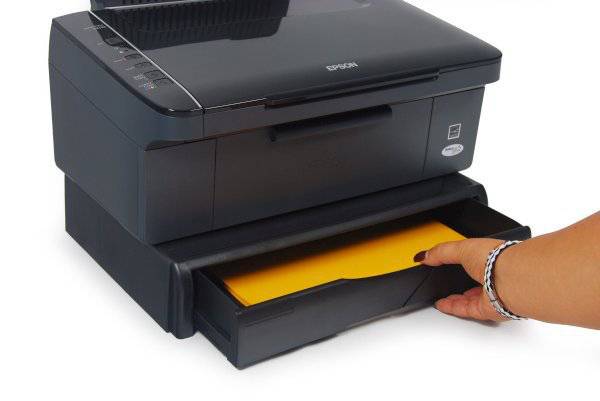 Eine Hand nimmt ein gelbes Blatt aus dem Papierfach eines schwarzen Epson-Druckers.