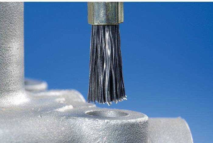 Ein Bürstwerkzeug reinigt ein Loch in einer Metalloberfläche und deutet auf einen industriellen oder fertigungstechnischen Kontext hin.