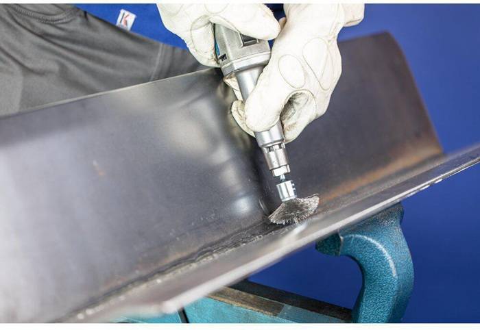 Eine Person mit Handschuhen verwendet ein Rotationswerkzeug, um eine Metallkante zu schleifen, was auf Metallbearbeitung oder Oberflächenveredelung hinweist.