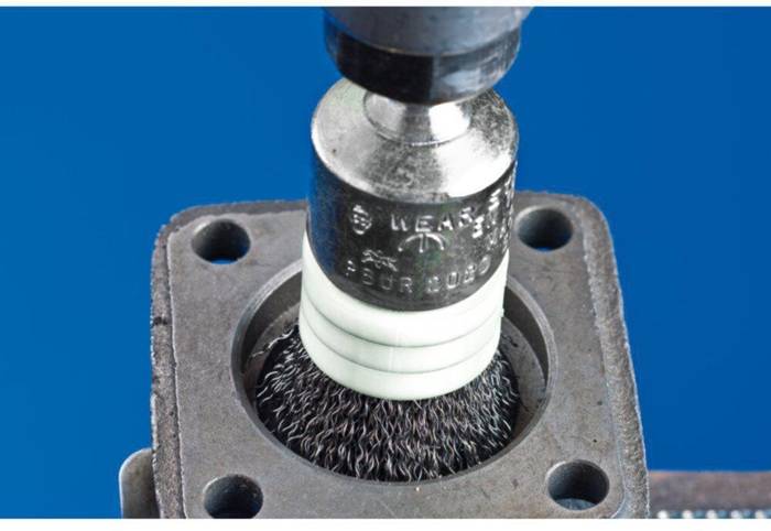 Ein Metallbürstengerät wird in eine quadratische Metallkomponente mit abgerundeten Ecken eingesetzt, was industrielle Reinigung oder Politur veranschaulicht.