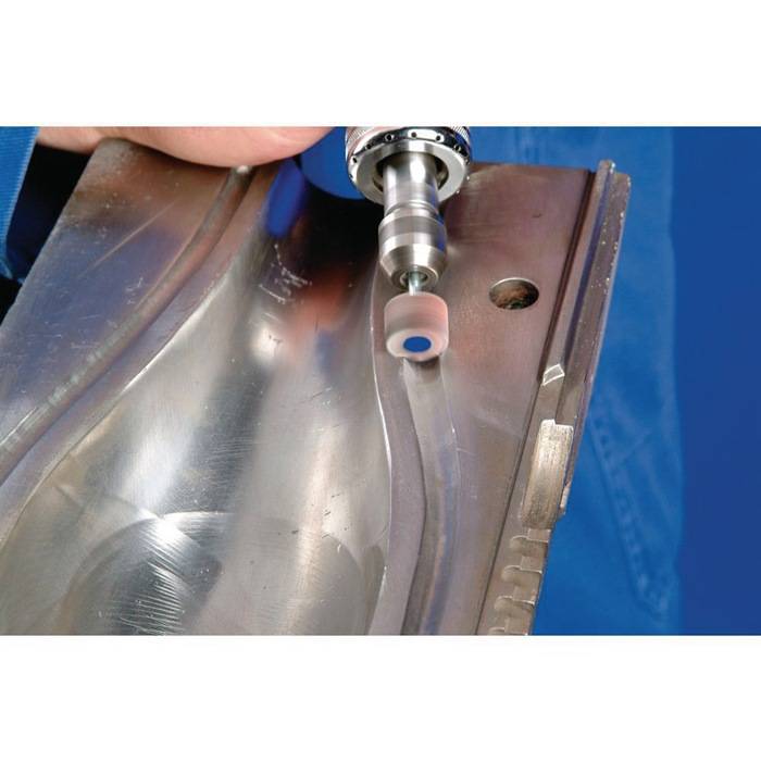 Eine Person, die ein Elektrowerkzeug verwendet, um die Kante eines Metallblechs zu polieren oder zu schleifen. Das Werkzeug hat eine rotierende zylindrische Anbaueinheit.